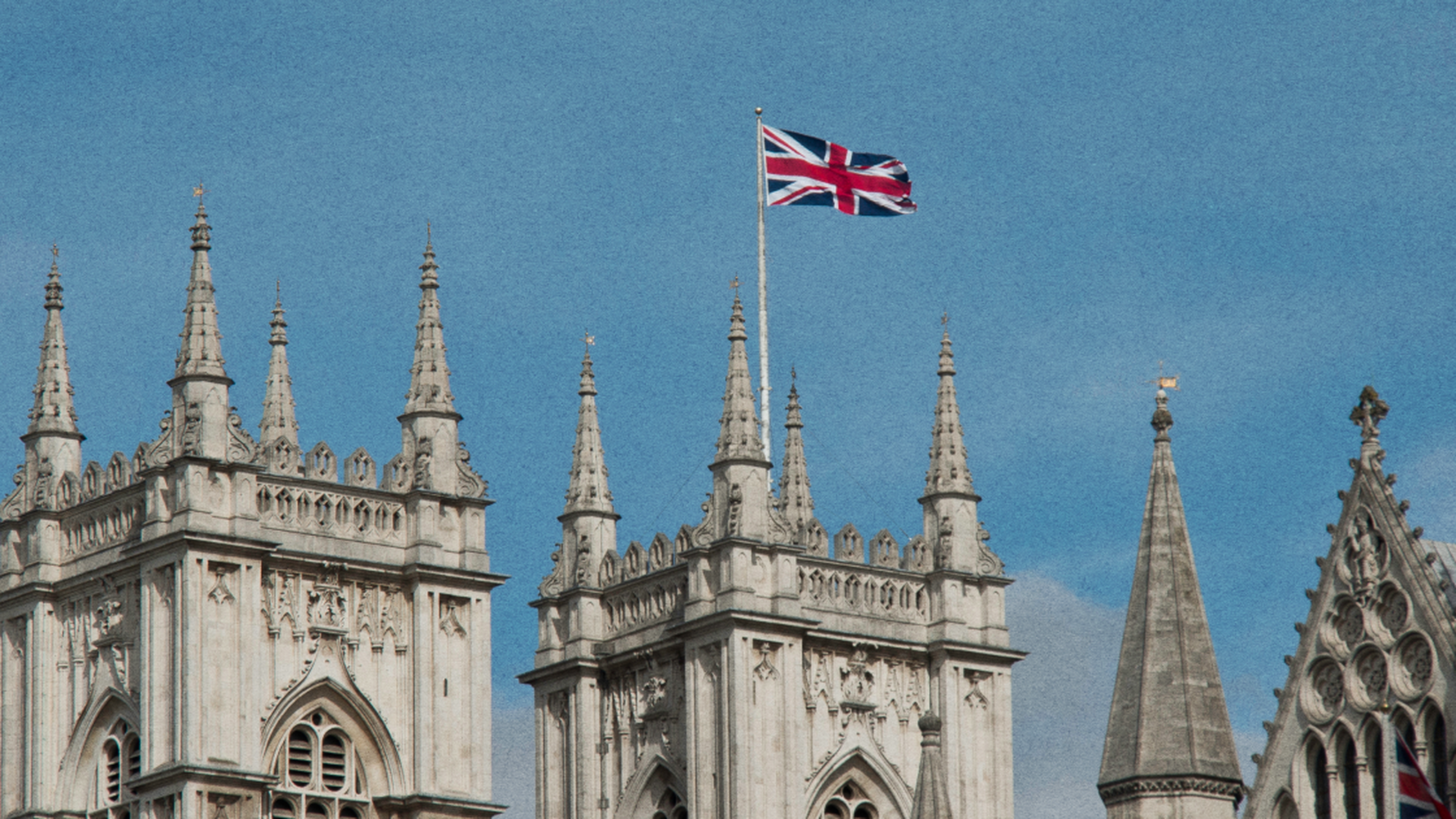 Gothic-style towers with intricate detailing and a British flag waving against a clear blue sky.