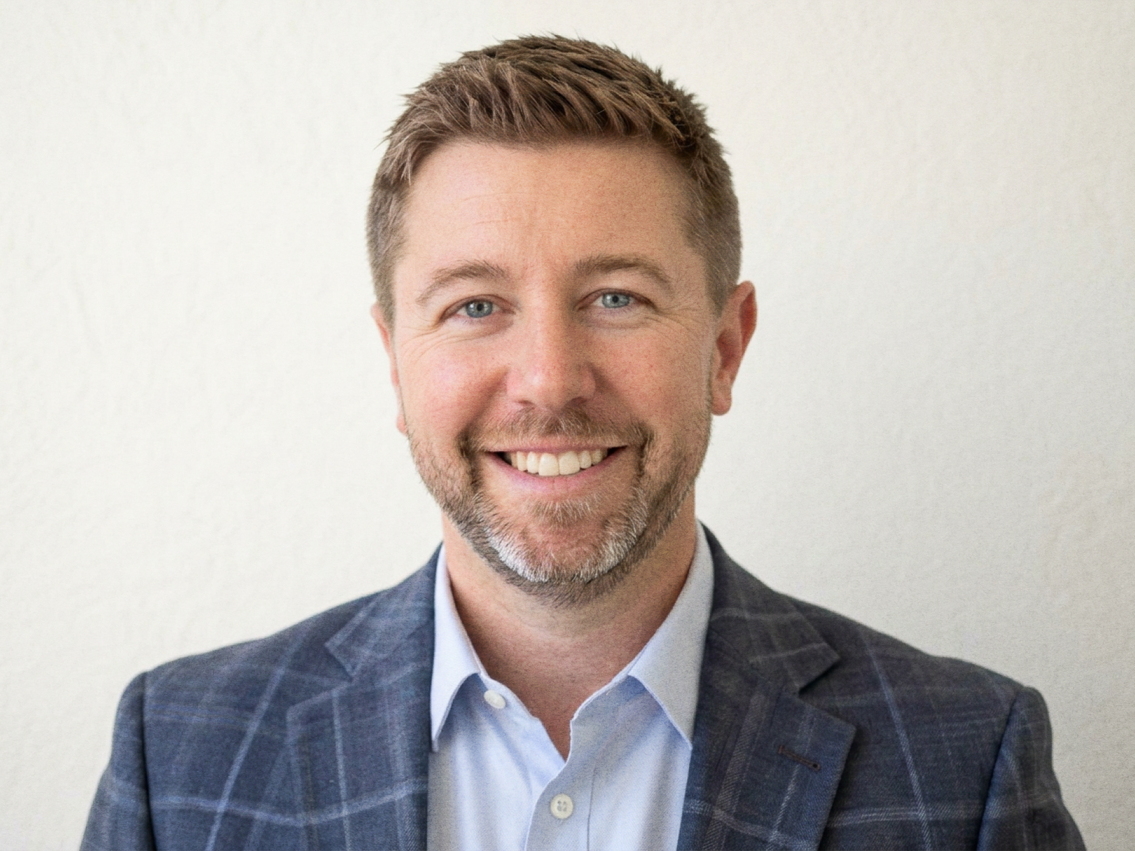 A headshot of Matthew Domeyer. A caucasian male with short blonde hair and short facial hair wearing a navy plaid suit with a light blue shirt.