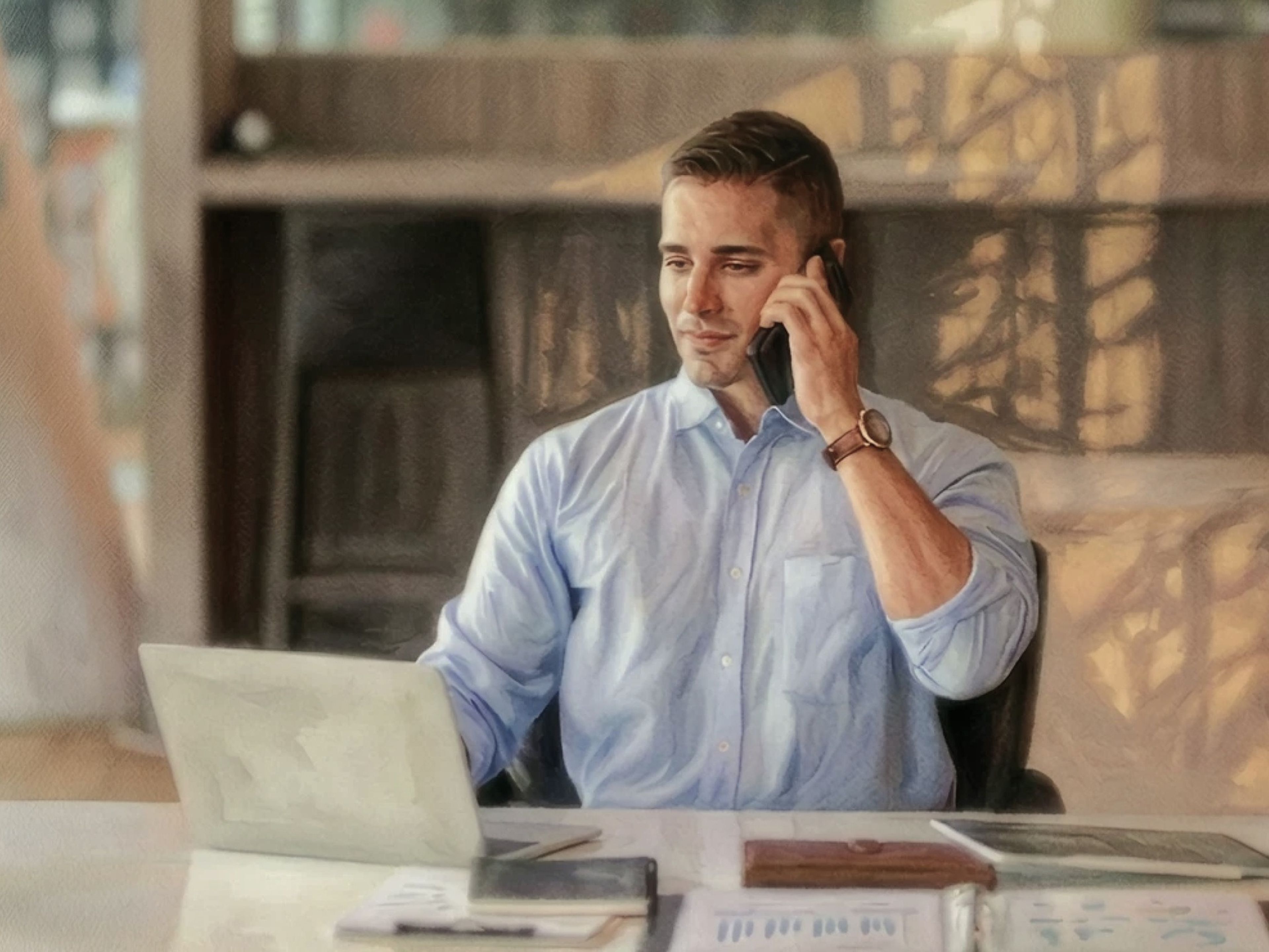 Man in blue shirt on the phone and working on a laptop
