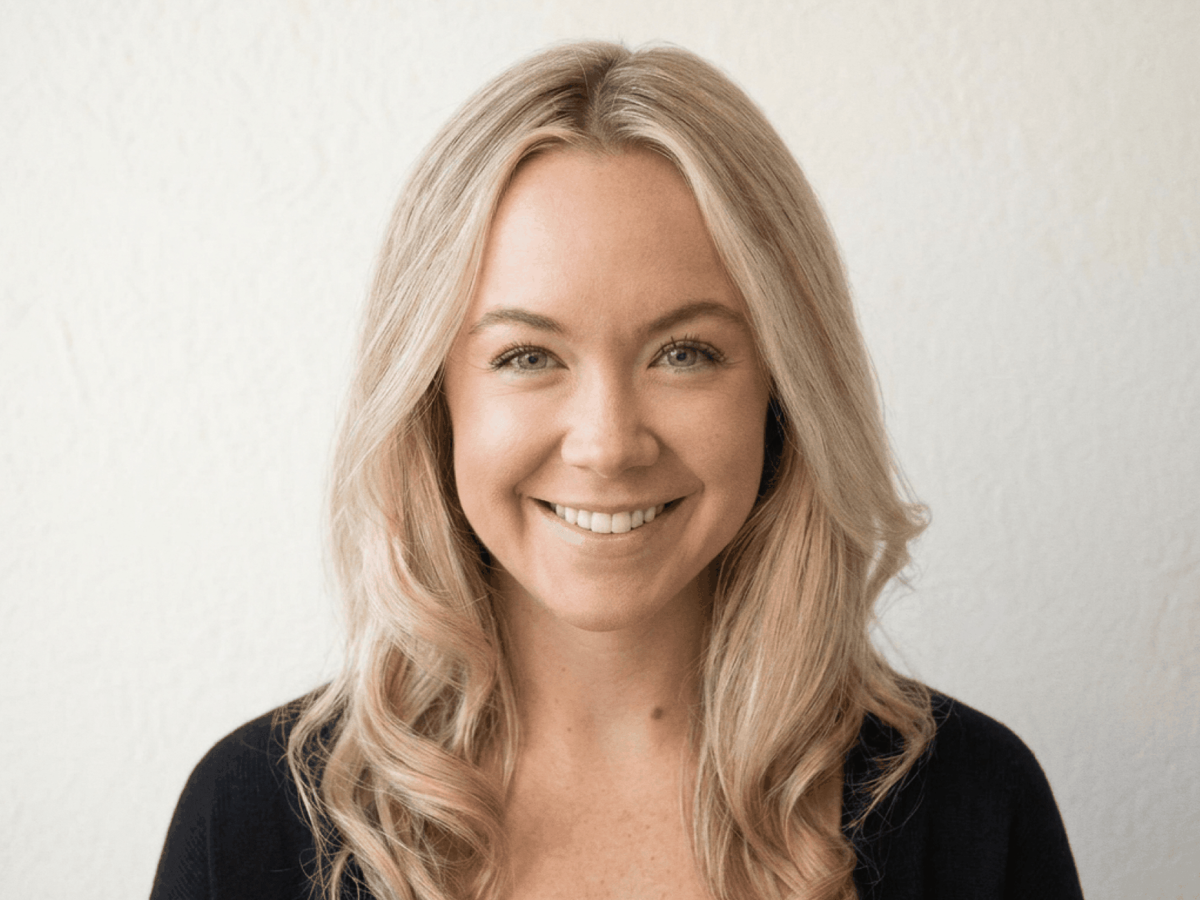 A headshot of Brittani Morelli. A caucasian woman with long blonde wavy hair, wearing a ran sweater.
