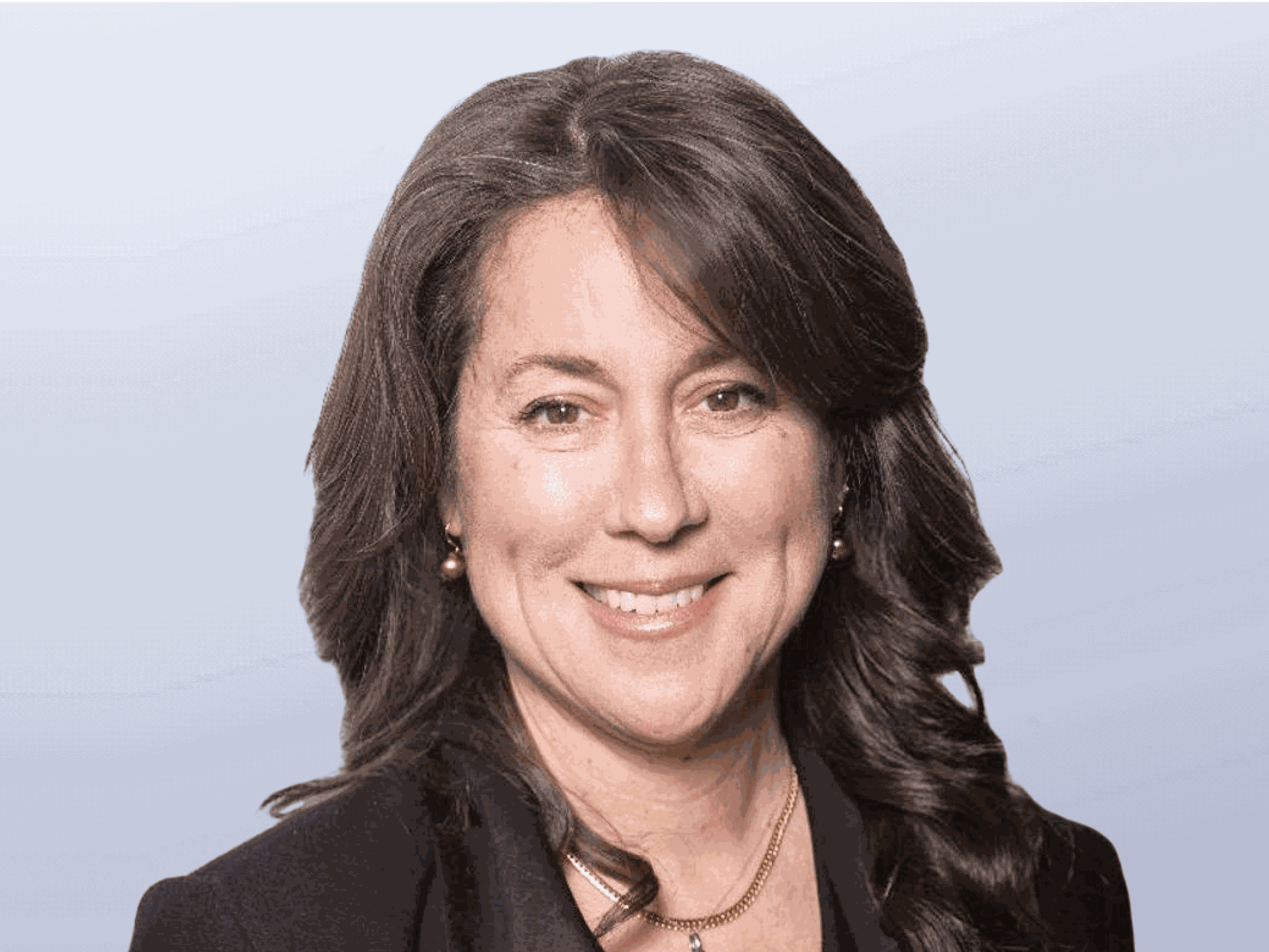 A headshot of Katherine Fleming. A caucasian woman with long, curly brown hair wearing a black blazer.