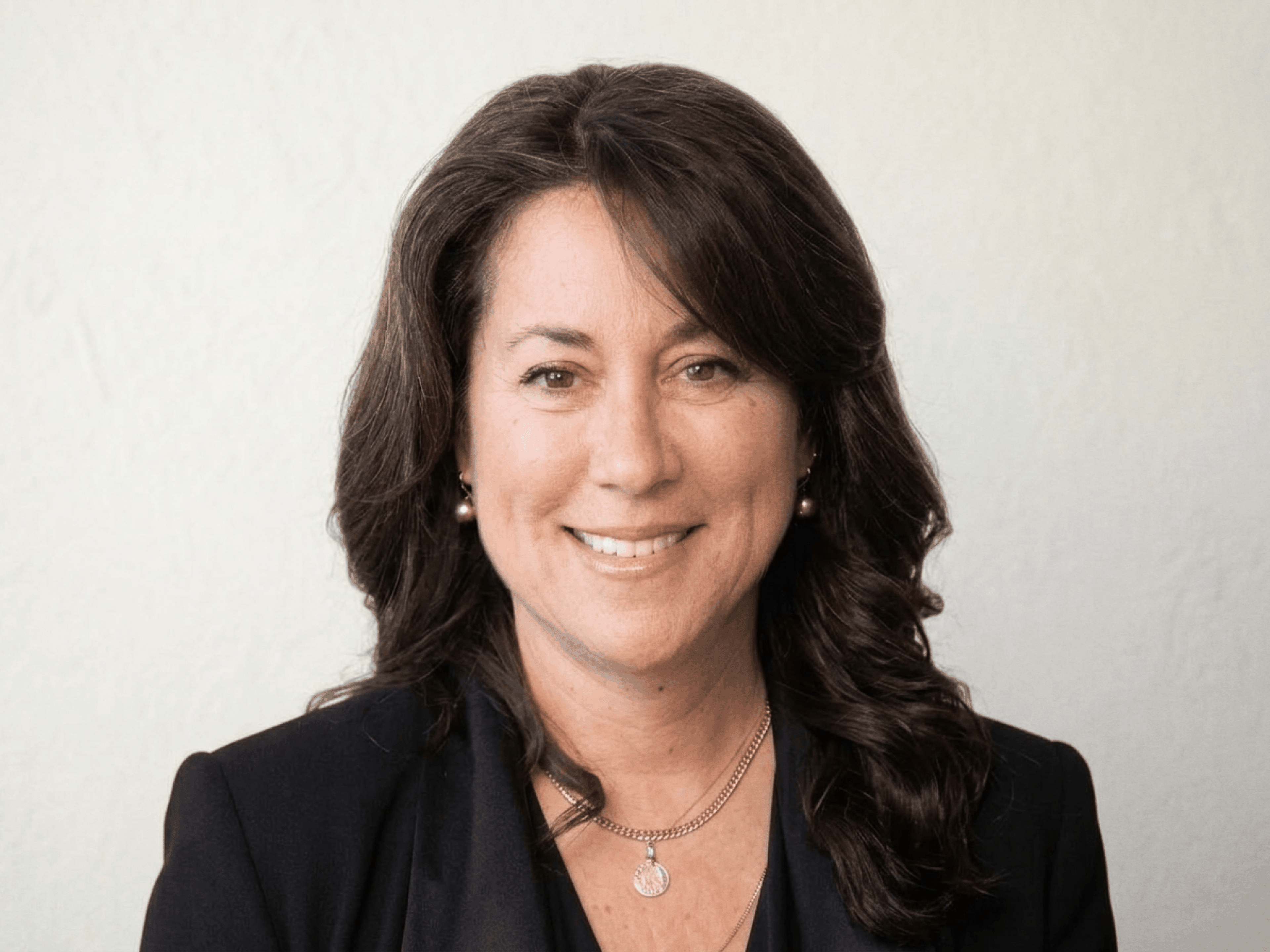 A headshot of Katherine Fleming. A caucasian woman with long, curly brown hair wearing a black blazer.