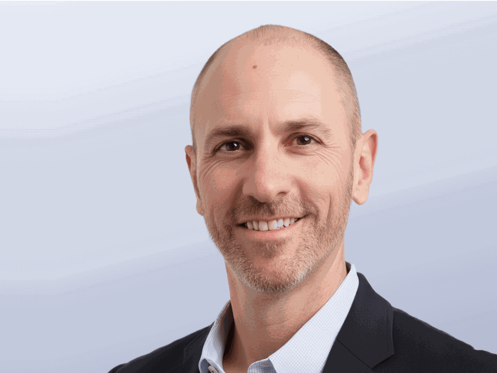 A headshot of Jamil Tahir. An arab male with no hair wearing a black suit and white shirt.