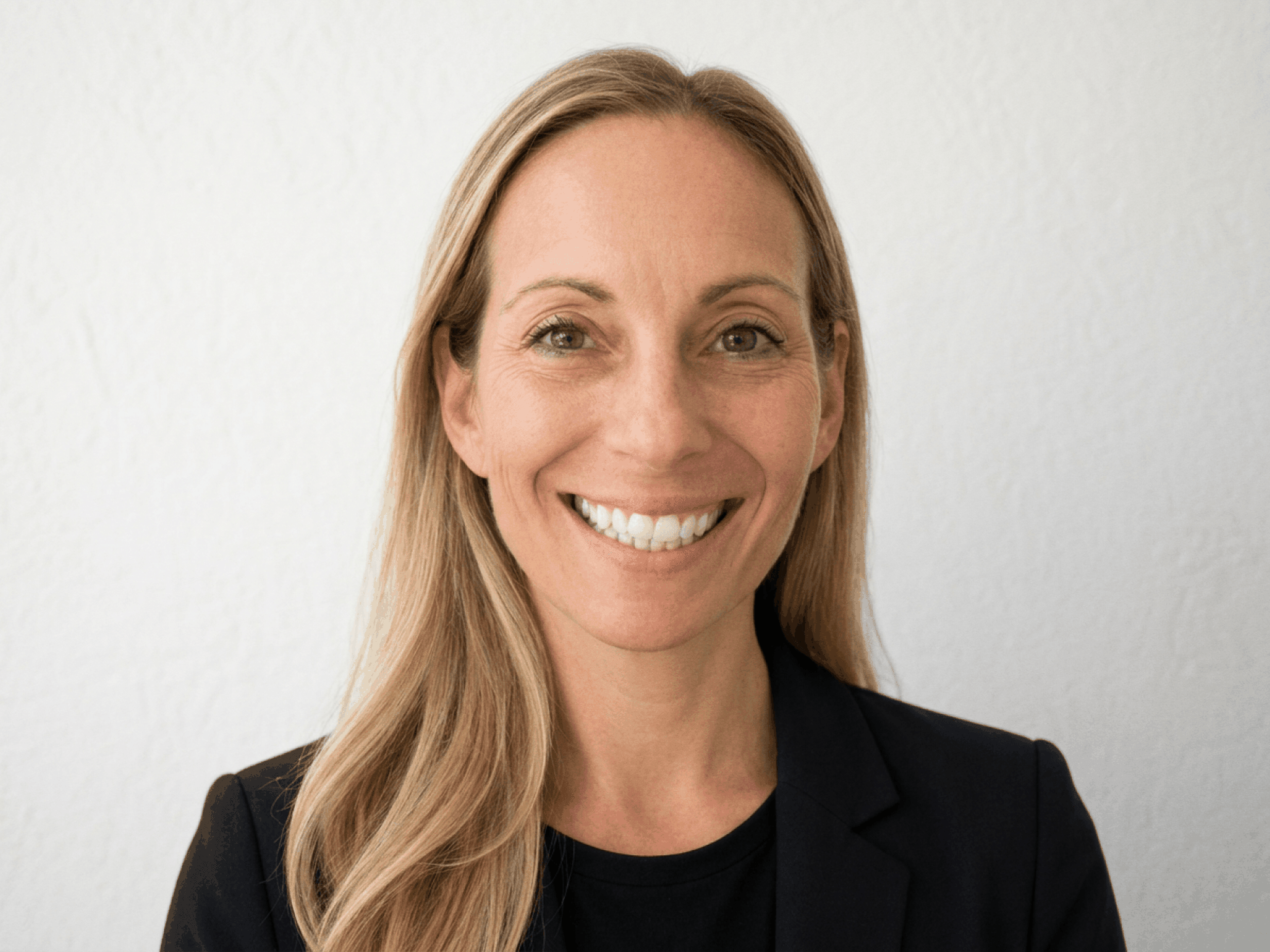 A headshot of Kelly Georgevich. A caucasian woman with long blonde hair wearing a black blazer.