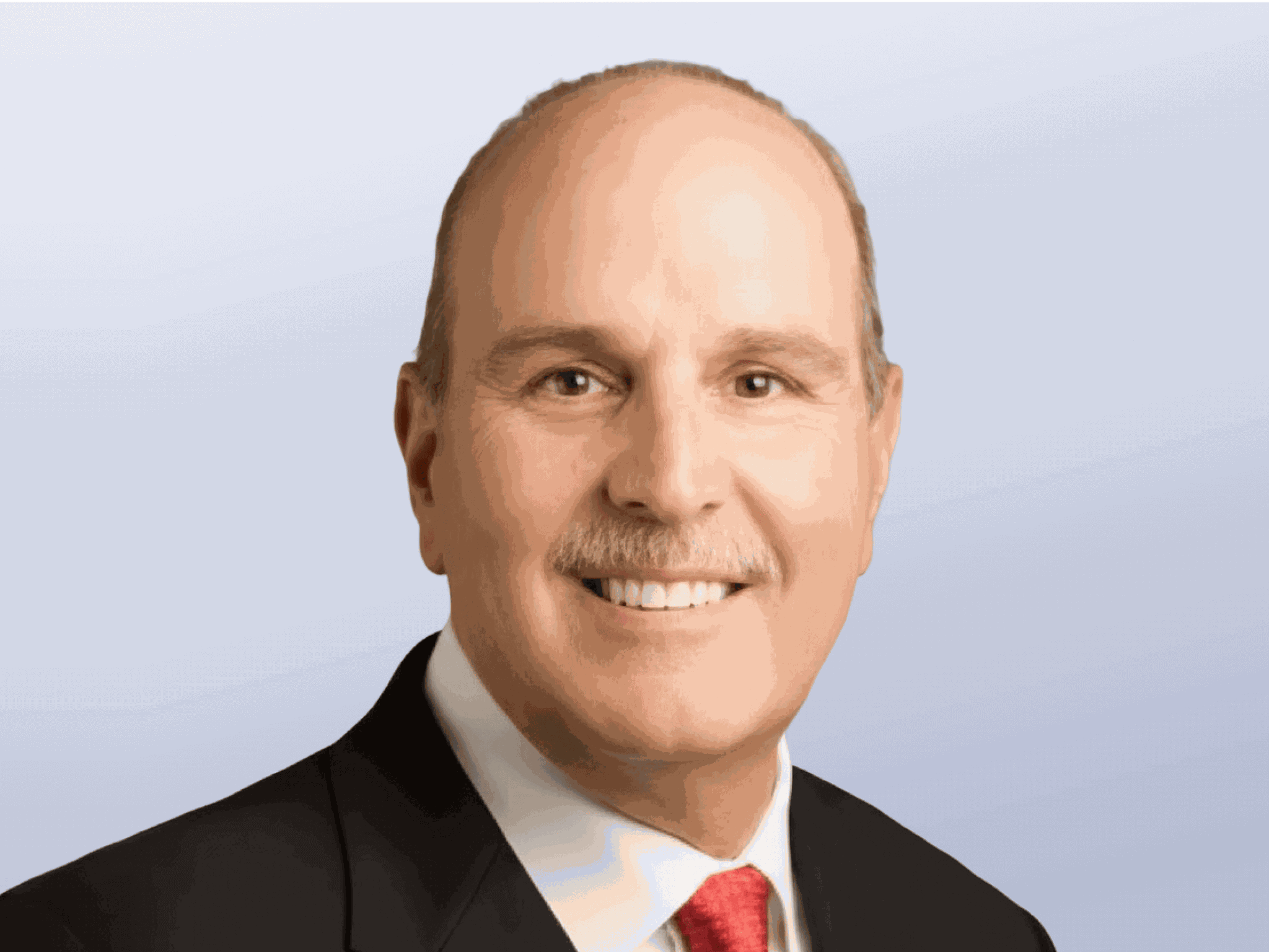 A headshot of Jim Hawkins. An older caucasian man with short hair and a mustache wearing a black suit.