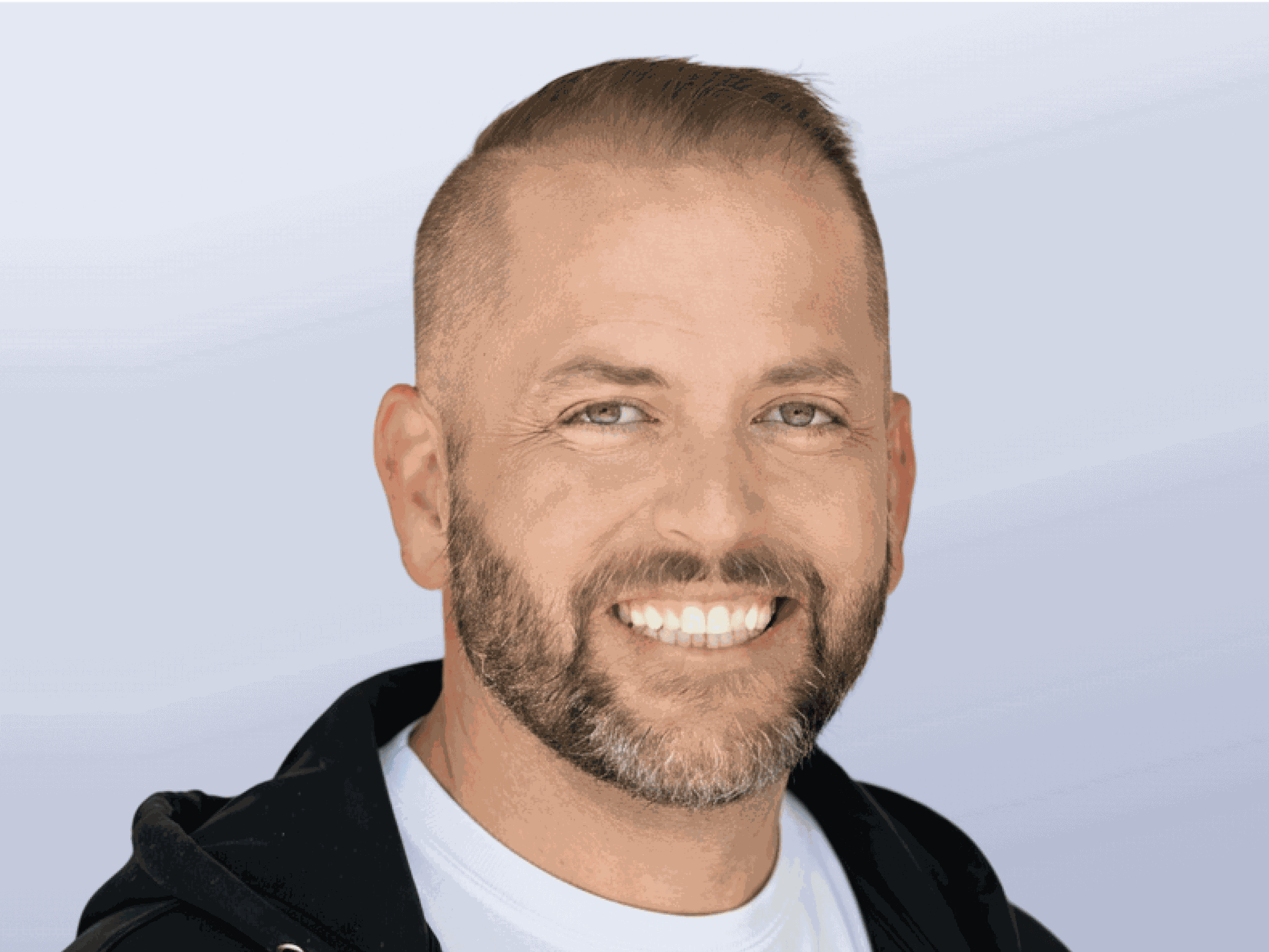 A headshot of Chad Sollis. A caucasian male with short blonde hair and short facial hair wearing a black zip-up jacket.