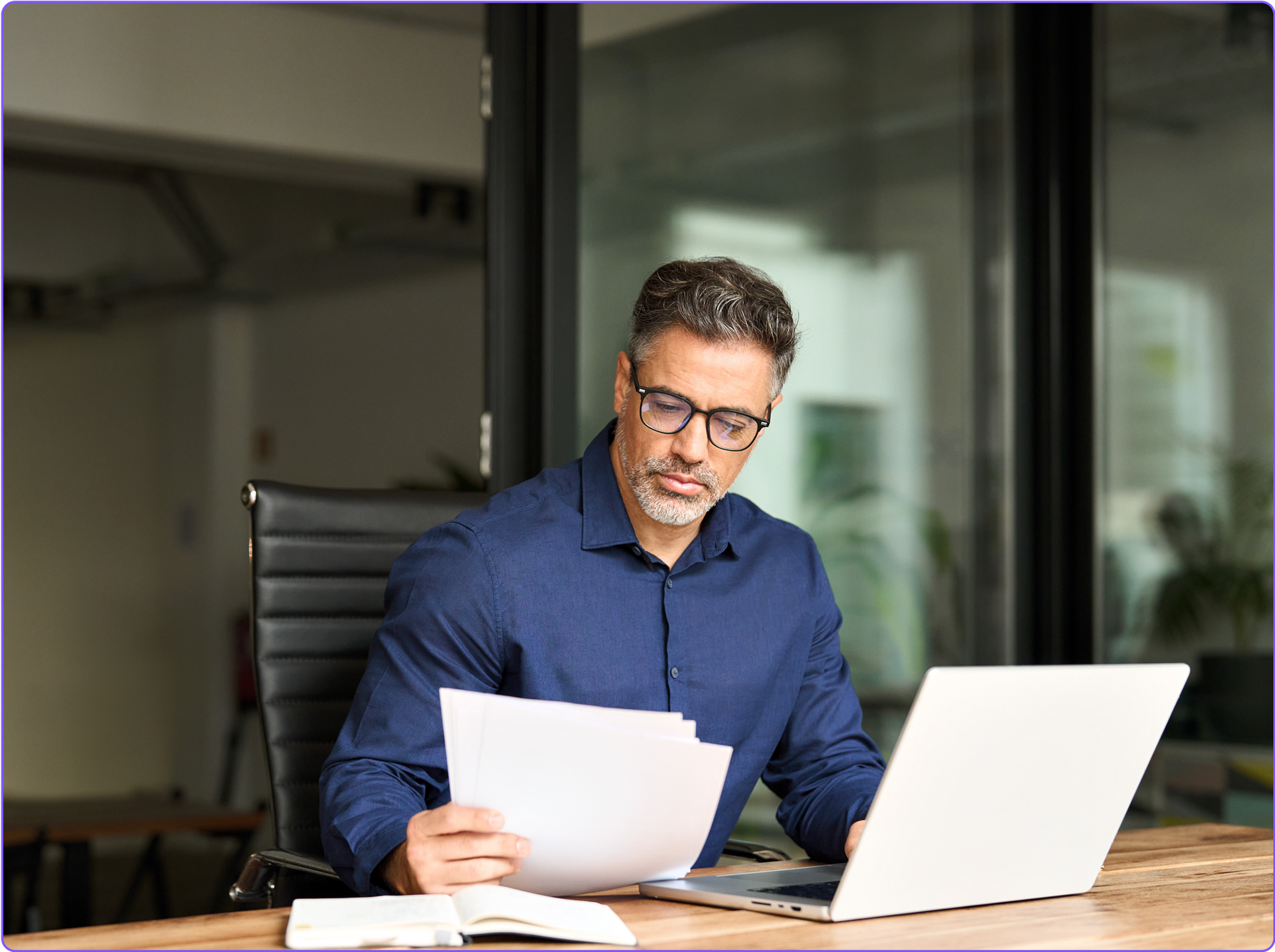 A company executive working on his laptop and reviewing paperwork.