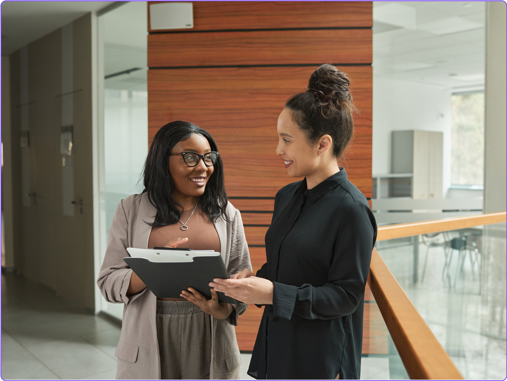 Two compliance managers chatting together in an office hallway.