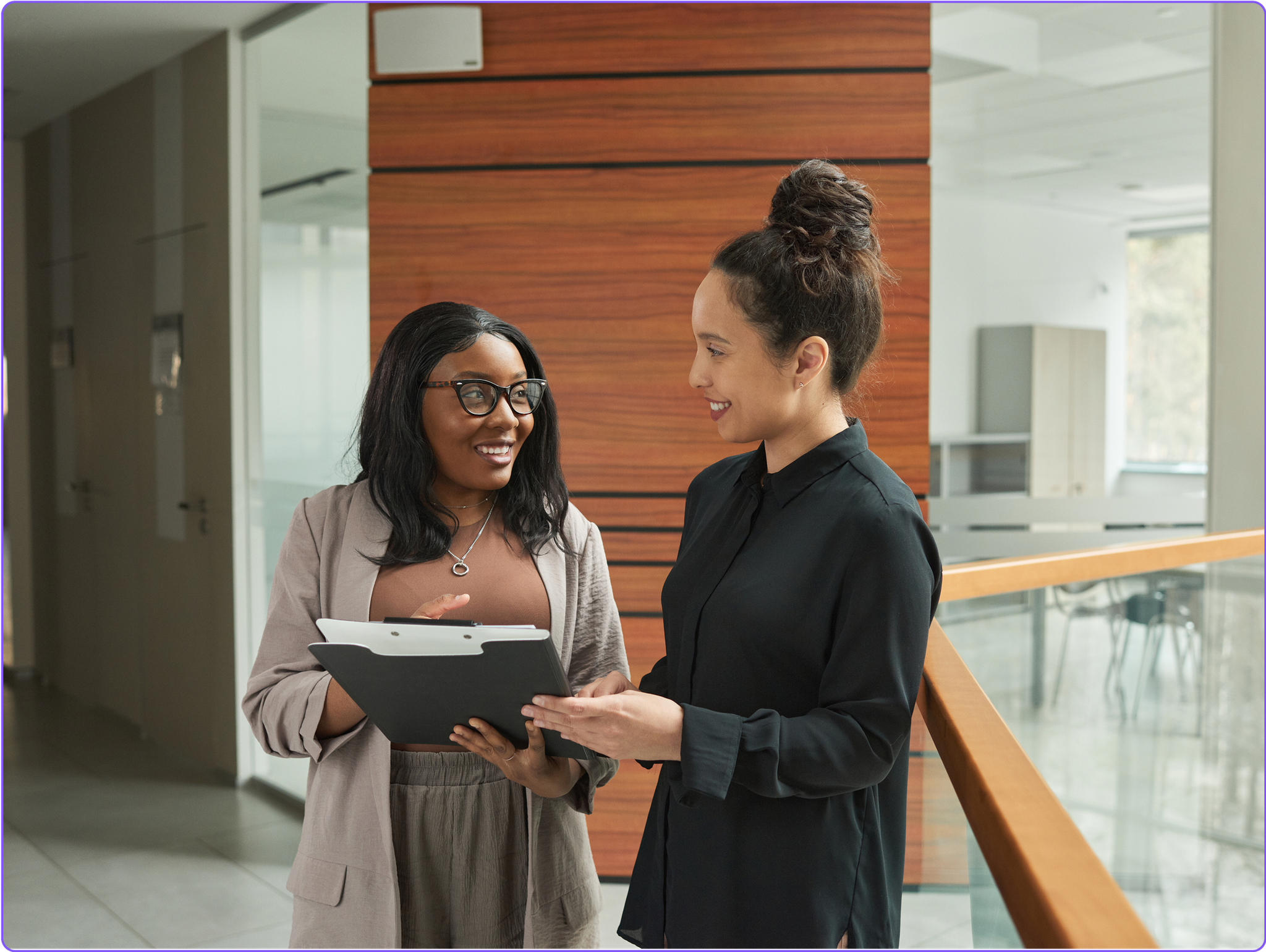 Two compliance managers chatting together in an office hallway.