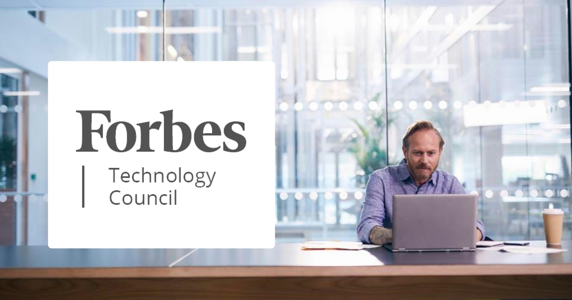 Man sitting at a desk typing on a laptop in front of large glass windows with the Forbes Technology Council logo on top.