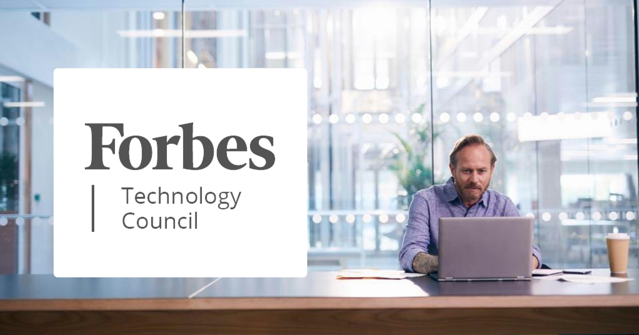 Man sitting at a desk typing on a laptop in front of large glass windows with the Forbes Technology Council logo on top.