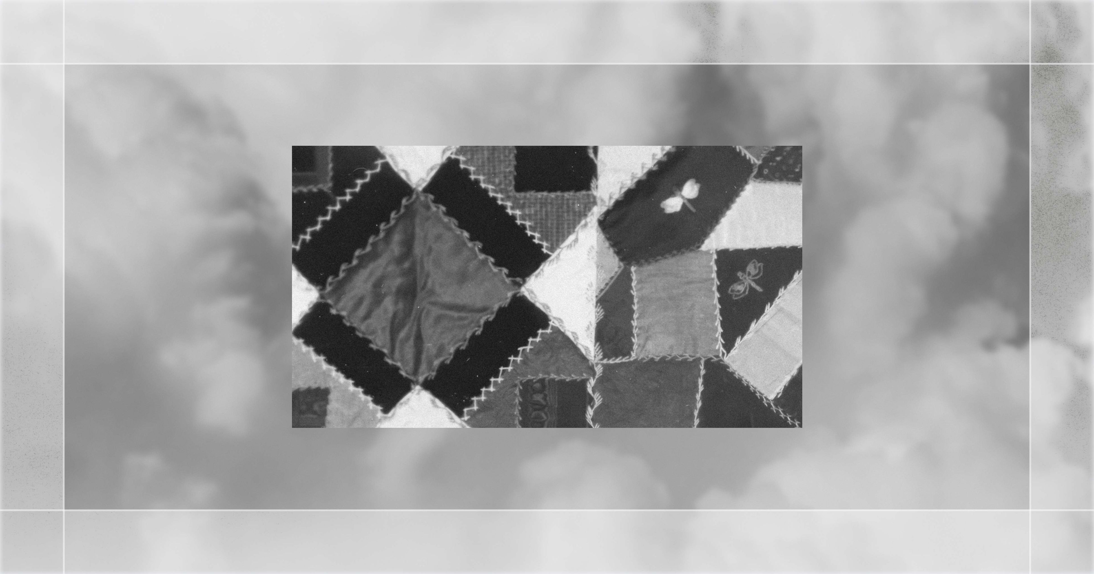 Patchwork quilt with various patterned and textured squares stitched together, featuring butterfly motifs, set against a cloudy background.