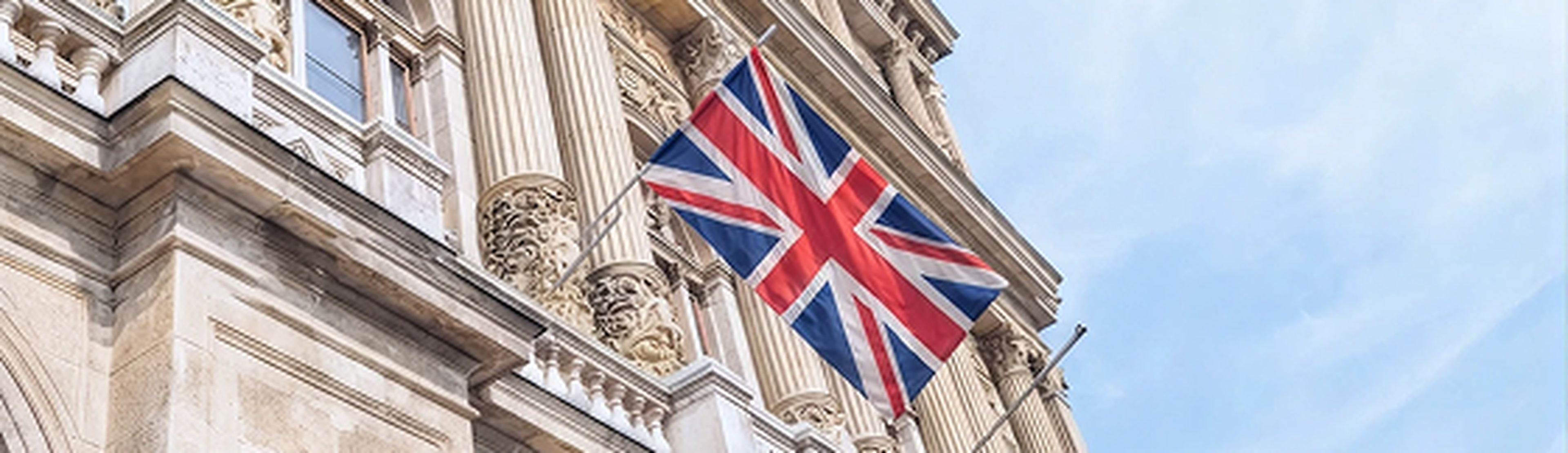 The Union Jack flag flies in front of an ornate building with columns.