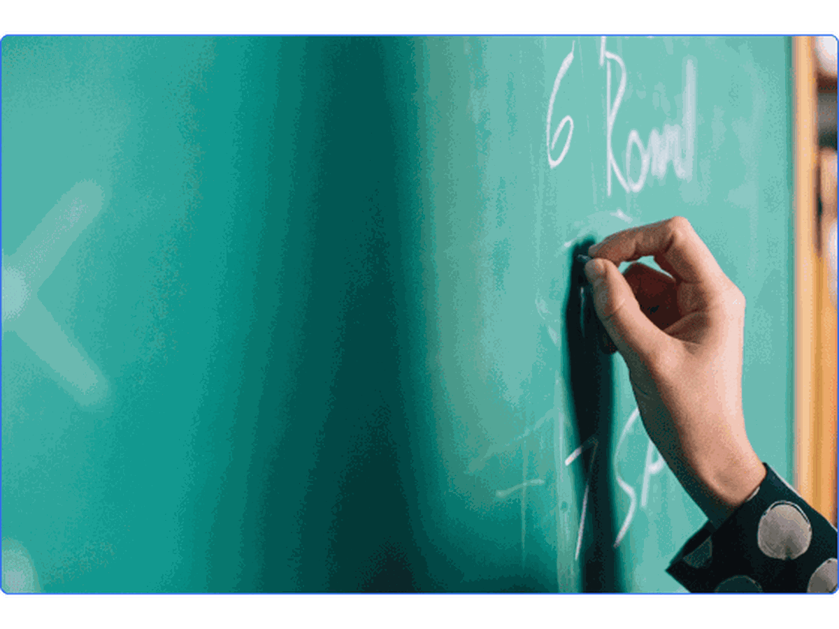 A teacher writing on a green chalkboard with white chalk.