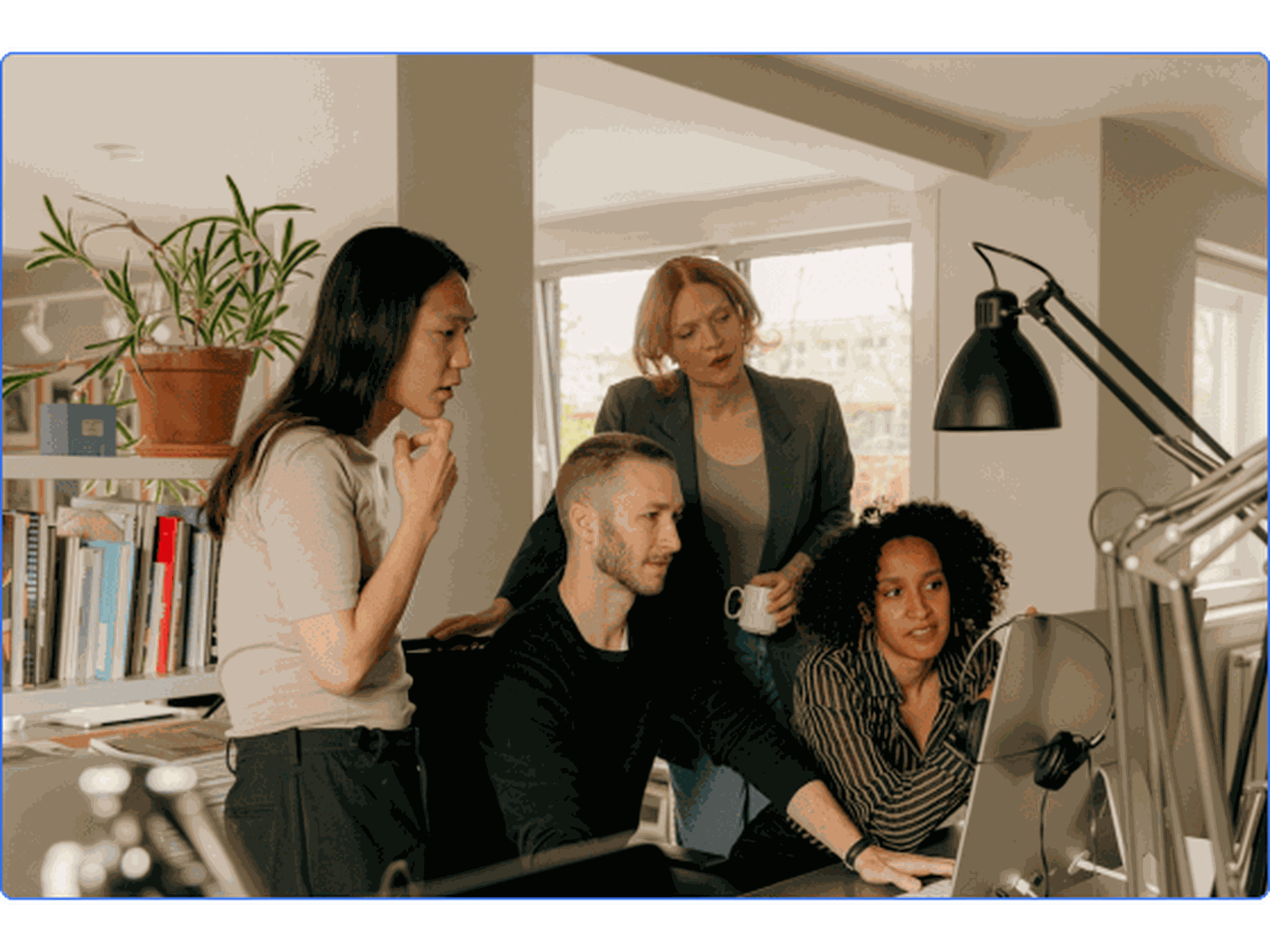 Team of four huddled around a computer collaborating on a project.