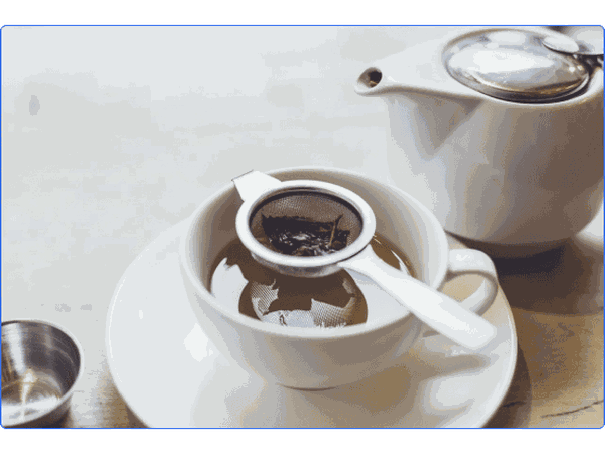 A white mug and teapot with loose leaf tea steeping.