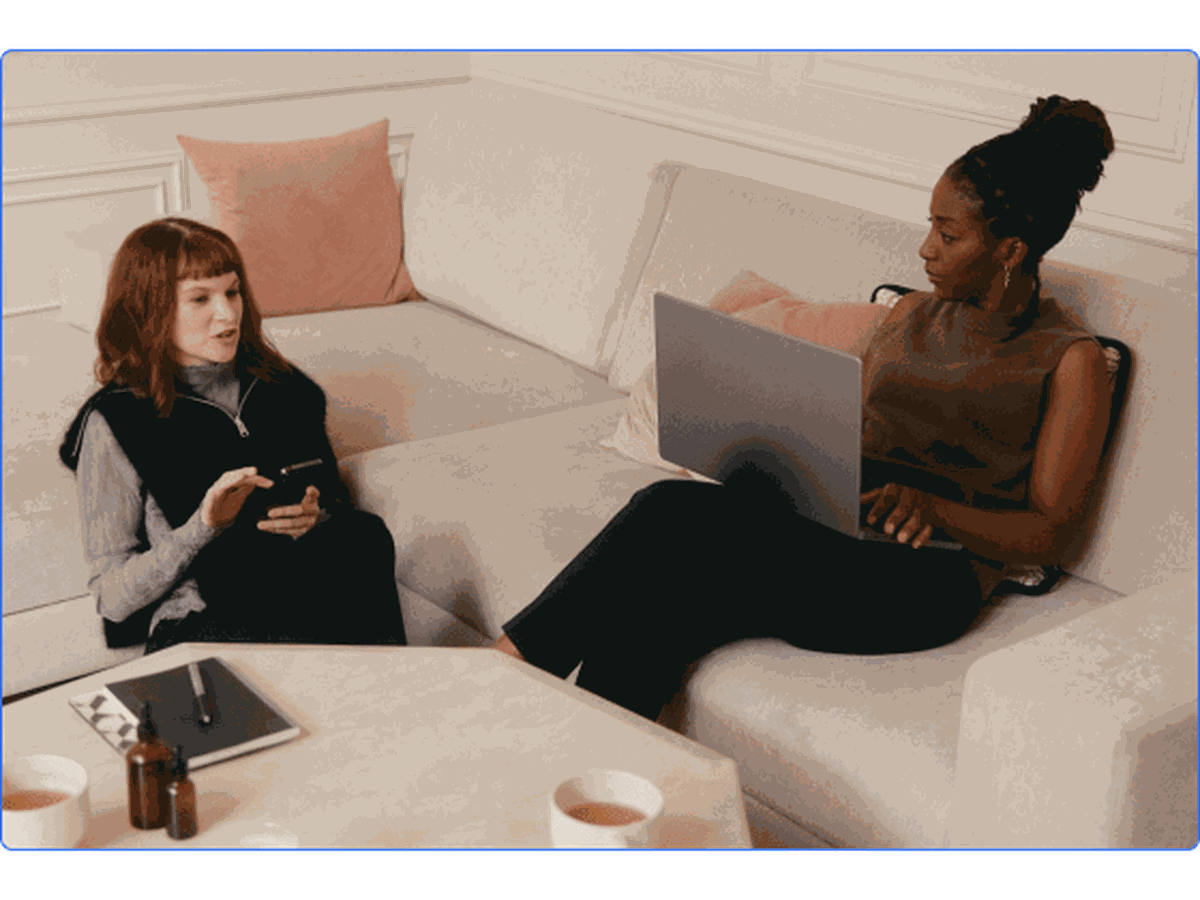 Two women collaborating on their laptops and phones.